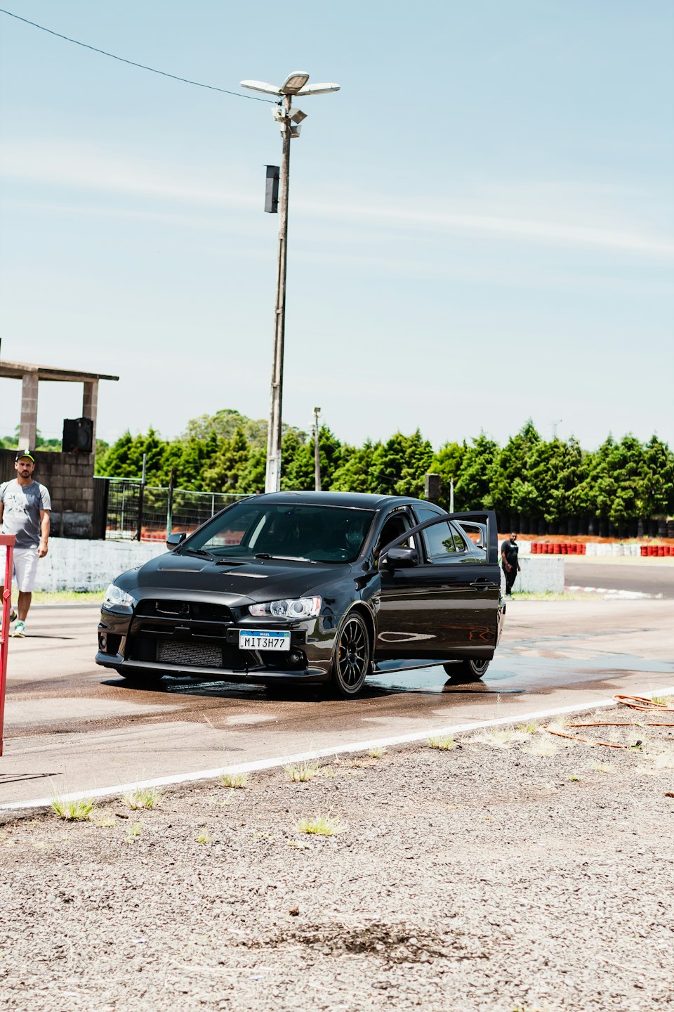 Man stands beside open-doored sports car on a race track.
